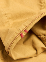Close-up of yellow cotton stretch fabric with visible stitching and a seam, plus a hint of red thread on the hem—details from the BGpaulo Pavia Pant in Sunflower by Blue de Gênes, evoking vintage military-inspired chinos.