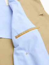 A close-up of the BGjacques Coat - Pale Khaki by Blue de Gênes highlights its beige heavy cotton fabric, light blue lining, interior pocket with brown trim, metal snap button, and a glimpse of a white tag.