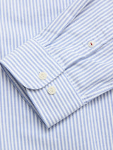 Close-up of the BGsander Oxford Shirt - Blue Stripe by Blue de Gênes, highlighting the cuff with two white buttons and sleeve. The 100% cotton fabric has thin vertical blue and white stripes for a crisp, clean look.