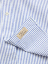 Close-up of the BGsander Oxford Shirt - Blue Stripe by Blue de Gênes, featuring blue and white stripes, 100% cotton Oxford fabric, a button detail, and a beige BYLOOM COTTON label sewn onto the pocket.
