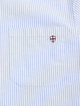 The BGsander Oxford Shirt - Blue Stripe by Blue de Gênes features light blue and white vertical stripes, a pocket with a small embroidered red cross shield logo, and is crafted from 100% cotton.