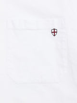 A close-up of the Blue de Gênes BGsander Oxford Shirt - White pocket, crafted from 100% cotton and detailed with a small embroidered shield featuring a red cross on white in the upper right corner.