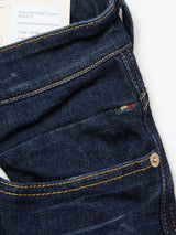 A close-up of Blue de Gênes Vinci Pala Dark V2 Jeans in dark blue stretch denim with yellow stitching, a brass rivet on the pocket, an Italian flag tag, and a partially visible clothing label at the waistband.