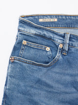 Close-up of Vinci Pala Used V2 Jeans by Blue de Gênes in denim blue, showing front pockets, copper rivets, a small shield patch, and an inner label reading Made in Italy with the Italian flag.
