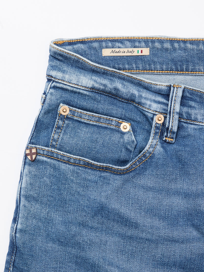 Close-up of Vinci Pala Used V2 Jeans by Blue de Gênes in denim blue, showing front pockets, copper rivets, a small shield patch, and an inner label reading Made in Italy with the Italian flag.