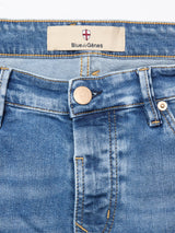 Close-up of the waist area of Vinci Pala Used V2 Jeans - Denim Blue by Blue de Gênes, featuring a metal button, belt loops, detailed stitching, and a beige label with the brand name and a small red and white shield logo above it.