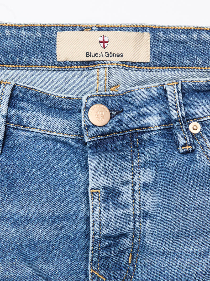 Close-up of the waist area of Vinci Pala Used V2 Jeans - Denim Blue by Blue de Gênes, featuring a metal button, belt loops, detailed stitching, and a beige label with the brand name and a small red and white shield logo above it.