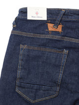 A close-up of the back pocket and waistband of Blue de Gênes Repi Dai V Dark V2 Jeans in dark blue denim, featuring yellow stitching, a Blue de Gênes tag in the waistband, and a small brown leather patch above the pocket.