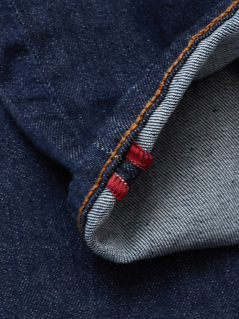 Close-up of durable dark blue denim on the Blue de Gênes Repi Dai V Dark V2 Jeans, featuring a rolled edge, orange stitching, and two red bar tacks highlighting classic five-pocket selvedge detail.