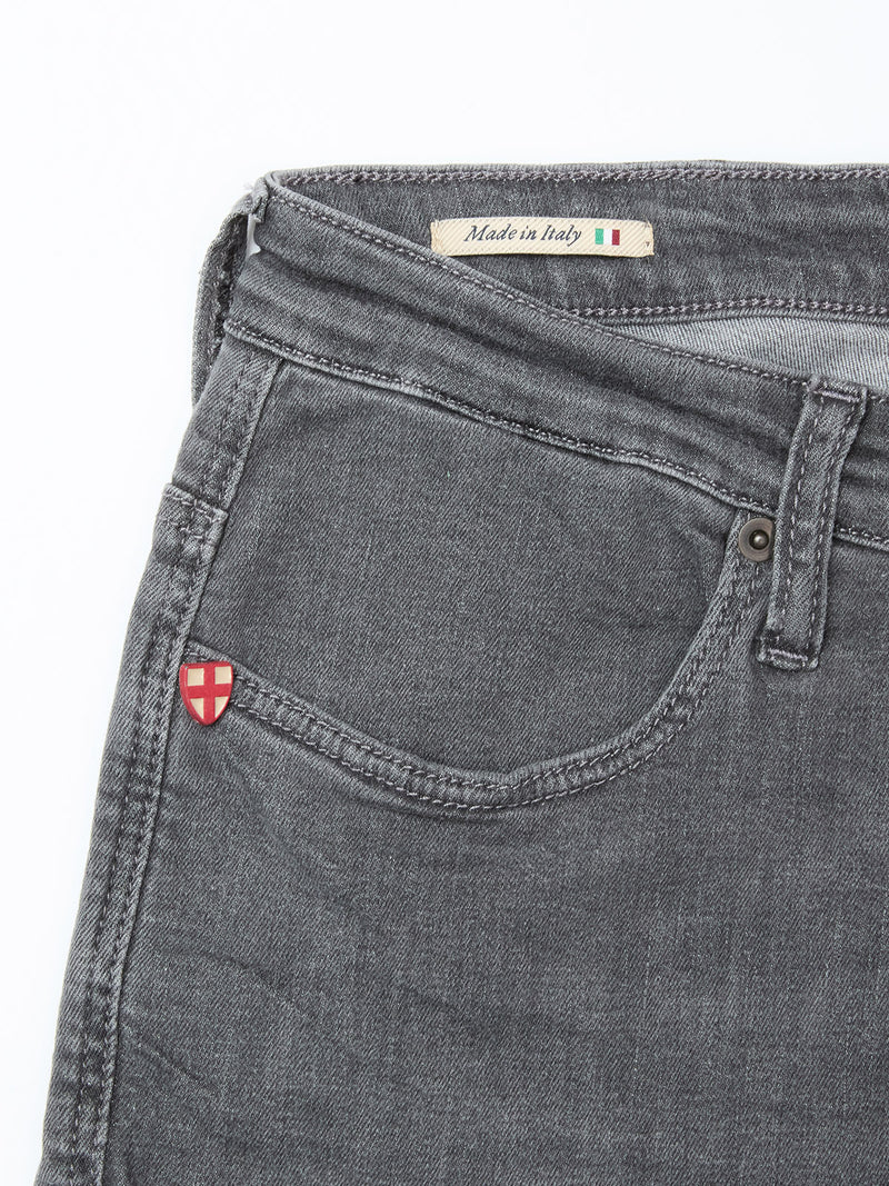 Close-up of the front pocket area of Blue de Gênes Repi Giulio Light V2 Jeans in grey denim, featuring a small red and white shield patch and a Made in Italy label, crafted from comfort stretch fabric for style and ease.