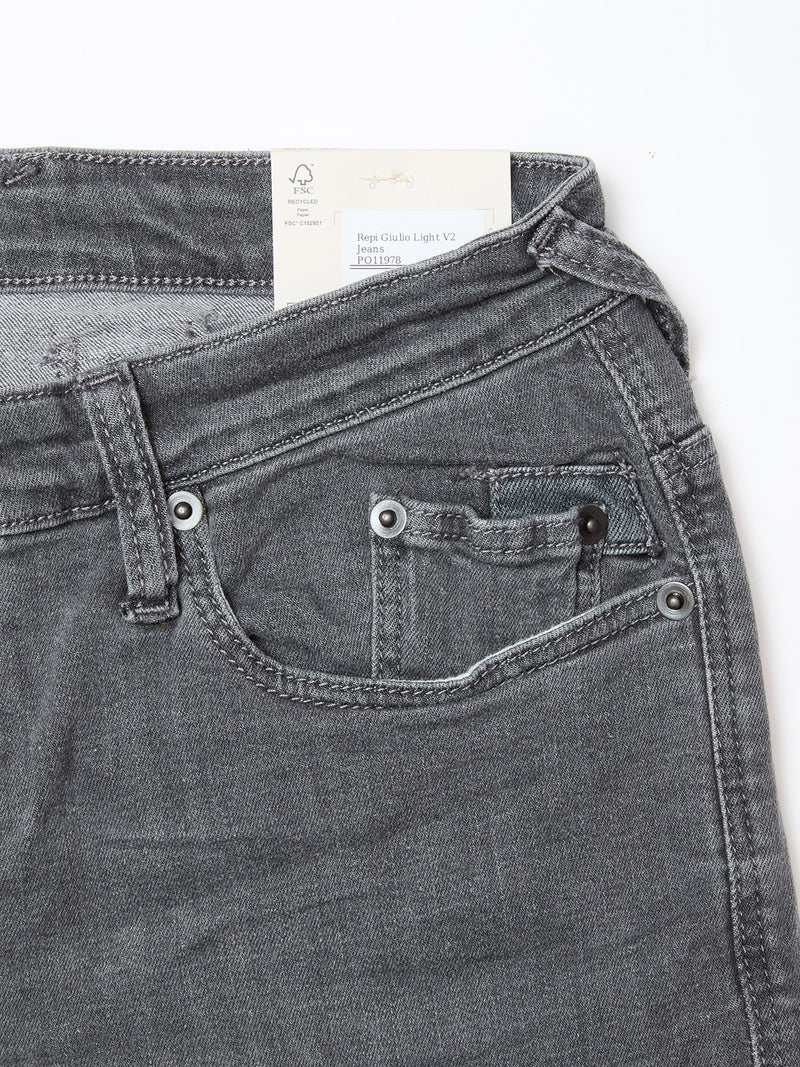 Close-up of the upper front section of Blue de Gênes Repi Giulio Light V2 Jeans in grey denim, highlighting the slim-fit waistband, front and coin pockets, belt loop, and a clothing tag inside the comfort stretch denim.