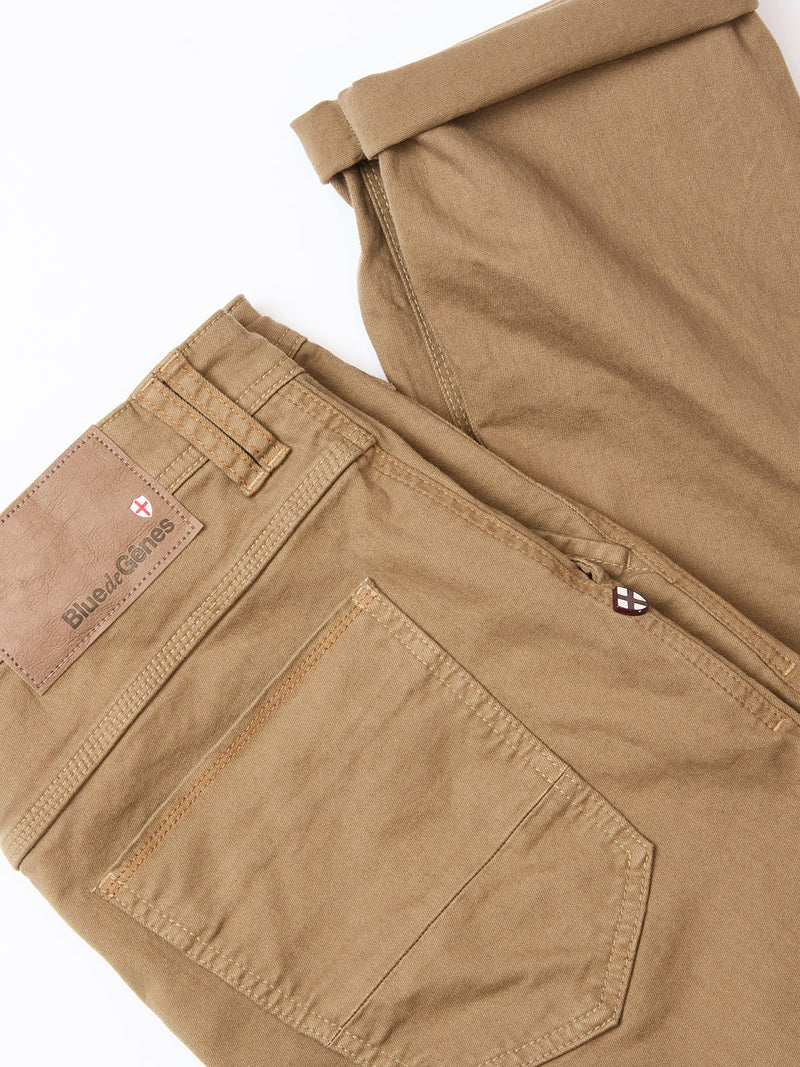 A pair of Paulo Pavia 1 V2 Chino pants in fudge by Blue de Gênes, featuring a visible back pocket, belt loops, a leather Blue de Gênes patch on the waistband, and crafted from soft cotton stretch fabric for comfort.