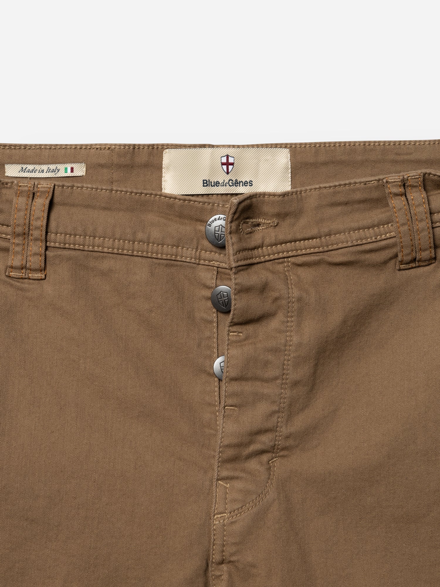 Close-up of BGpaulo Pavia 1 V2 Chino - Fudge pants by Blue de Gênes, featuring three metal buttons, front pockets, belt loops, and a label with Italian and shield logos. Inspired by vintage military pants. Made in Italy.