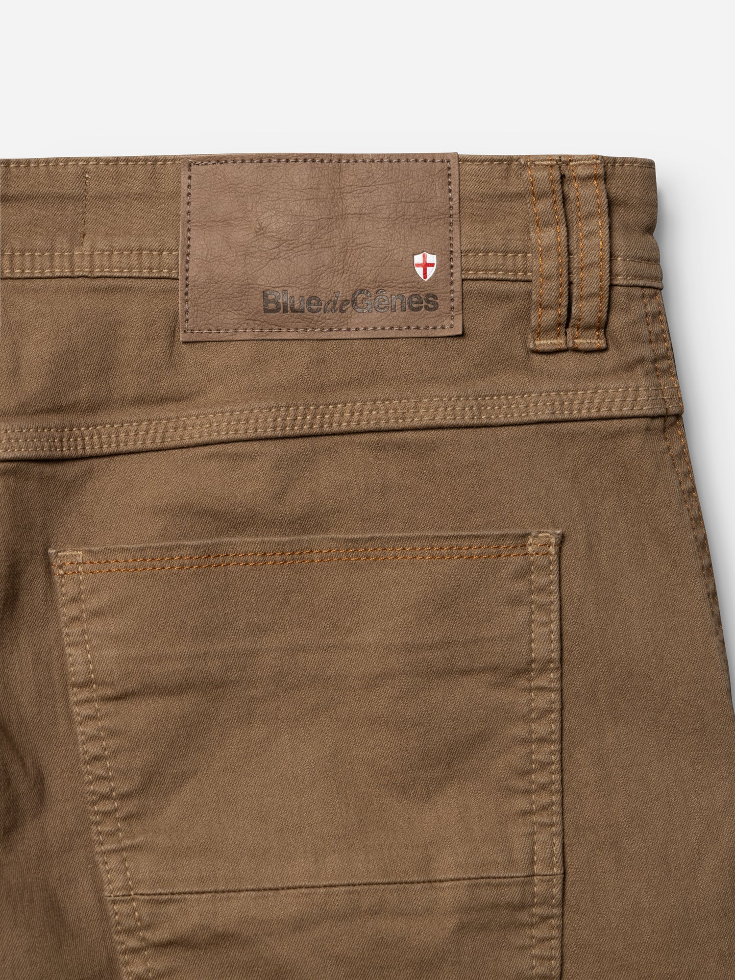 Close-up of the back pocket and waistband of Blue de Gênes BGpaulo Pavia 1 V2 Chino - Fudge, featuring a leather brand patch and a red-and-white shield emblem, inspired by vintage military pants.