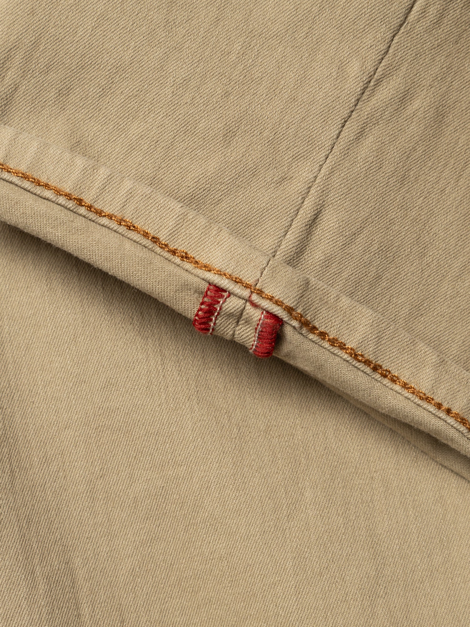 Close-up of tan cotton stretch fabric from Blue de Gênes BGpaulo Pavia 1 V2 Chino - Khaki, featuring two intersecting seams with orange stitching and red thread reinforcement, highlighting the garment’s durable construction.
