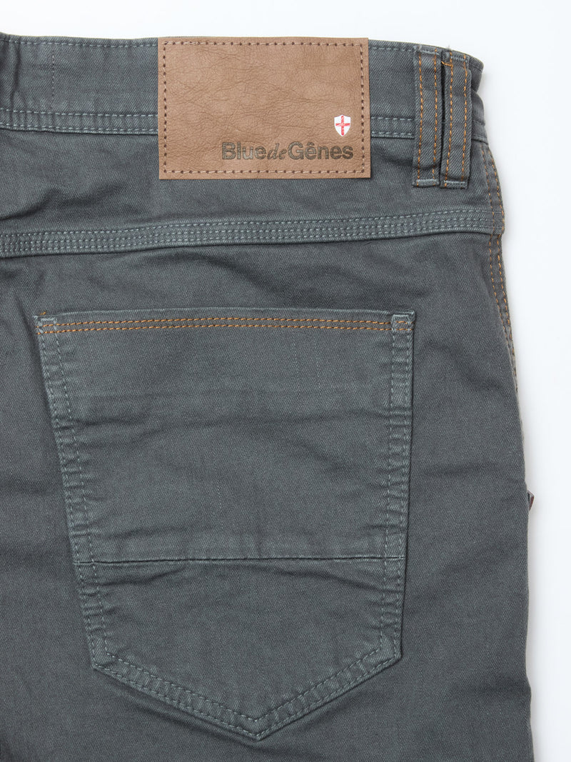 Close-up of the back pocket and waistband of Blue de Gênes Paulo Pavia 1 V2 Chino - Charcoal, made from stretch cotton with brown stitching, a brown leather Blue de Gênes patch, and a small red and white shield logo above the pocket.