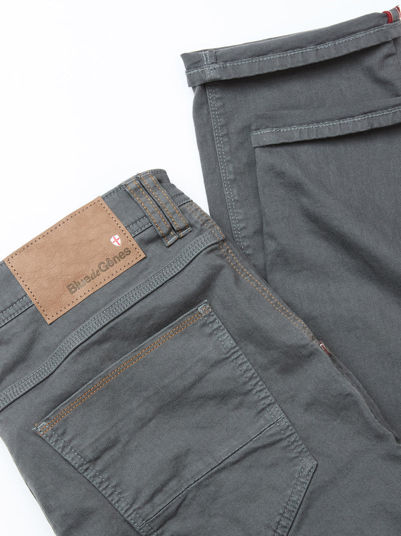 A close-up of two pairs of gray pants, including vintage military and Blue de Gênes Paulo Pavia 1 V2 Chino - Charcoal styles, with back pockets and a brown leather Blind Genes patch, displayed on a white background.