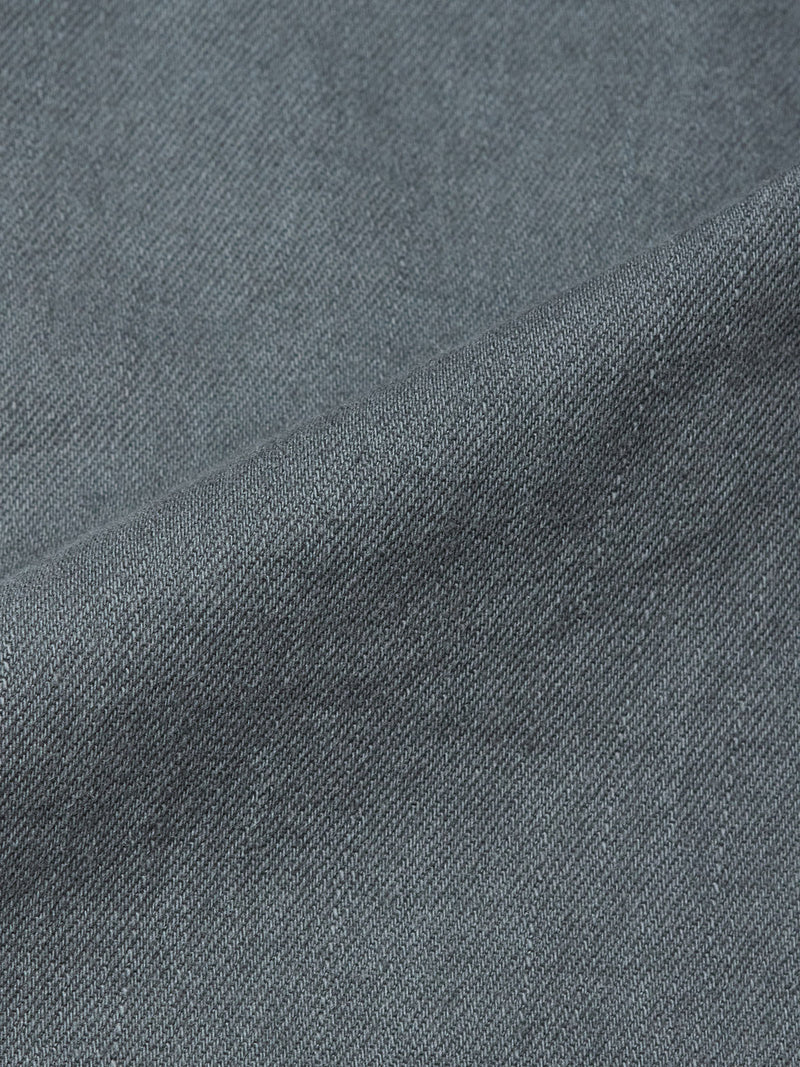 Close-up of Blue de Gênes Paulo Pavia 1 V2 Chino in charcoal shows its blue-gray denim fabric with a diagonal weave and subtle texture variations, reminiscent of vintage military pants, featuring a visible diagonal seam.