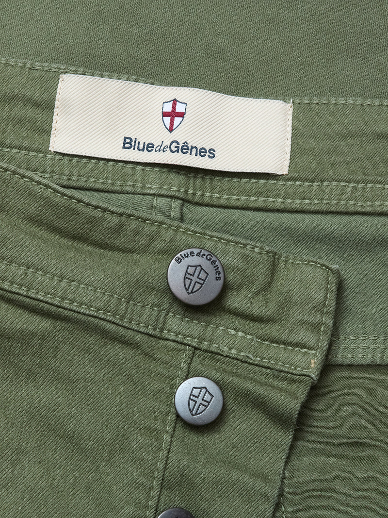 Close-up of the Paulo Pavia 1 V2 Chino in Army by Blue de Gênes, featuring metal buttons and a beige label with red and white shield logo above the waistband. Made from comfortable cotton stretch fabric for style and ease.