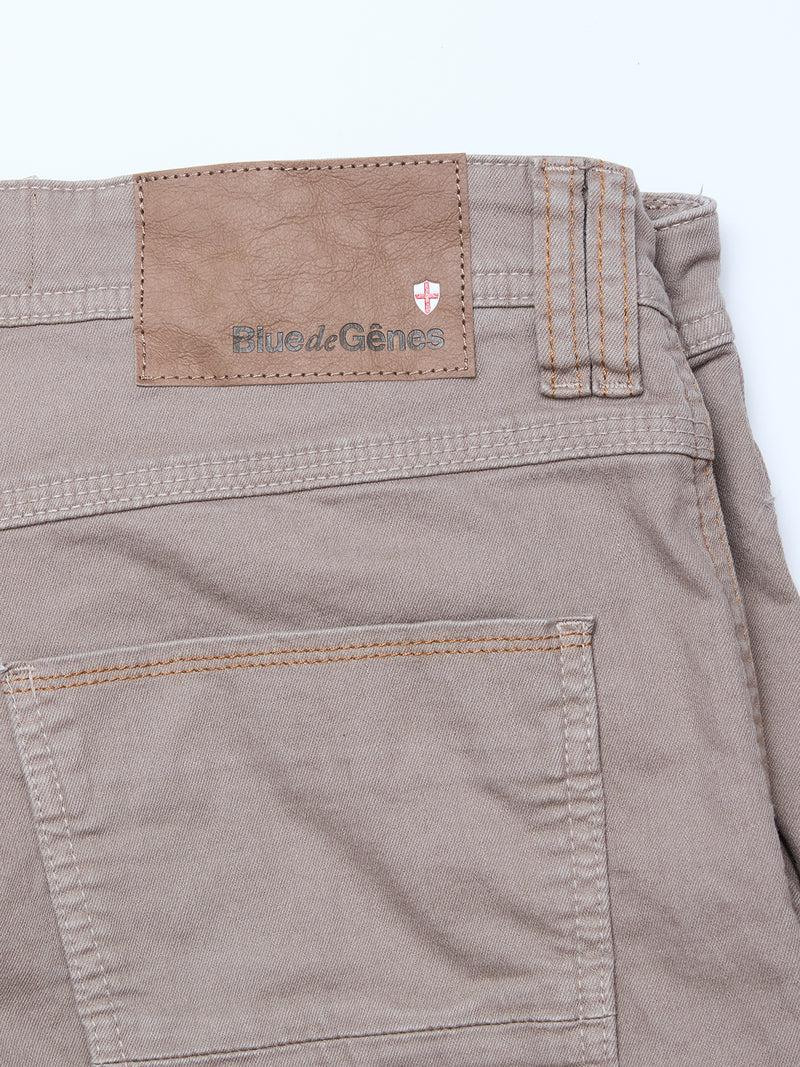 Close-up of the back of Blue de Gênes Paulo Pavia 1 V2 Chino - Fungi, showing a brown leather waistband patch with the brand name and red and white shield logo. Part of the back pocket is also visible.