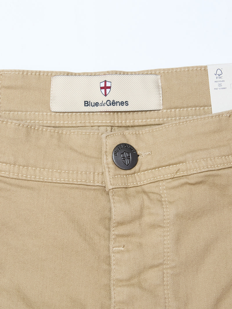 Close-up of the waistband of Blue de Gênes Paulo Pavia 1 V2 Chino in khaki, showing a metal button with engraved shield, a Blue de Gênes label with red and white shield logo, and a white care tag inside.