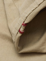 Close-up of the Paulo Pavia 1 V2 Chino in khaki by Blue de Gênes, showing beige cotton stretch fabric with visible stitching, a seam, and two small red thread accents at the hem.