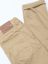 The Blue de Gênes Paulo Pavia 1 V2 Chino in khaki features a military-inspired design, brown leather patch, and a red and white shield logo near the back pocket, shown on a white background.