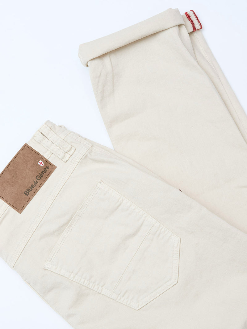 A pair of BGpaulo Pavia 1 V2 Chino pants in ecru by Blue de Gênes, neatly folded to show the brown leather “Blue Genes” patch and back pocket, crafted from cotton stretch fabric and displayed on a white background.