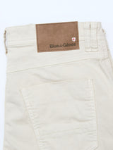 The BGpaulo Pavia 1 V2 Chino in ecru by Blue de Gênes is made from cotton stretch fabric, shown folded to display the back pocket and a brown leather logo patch with red and white shield, set against a clean white background.