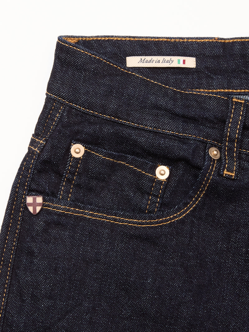 Close-up of Blue de Gênes Recco F V2 Jeans - Rinse Wash in dark blue denim with yellow stitching, metal rivets, a small pocket, and an Italian flag “Made in Italy” label inside the waistband; a crest adorns the front pocket.