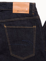 Close-up of the back pocket on Blue de Gênes Recco F V2 Jeans in a rinse wash, featuring yellow stitching and a tan leather patch with the brand name and a small red and white cross emblem above the pocket.
