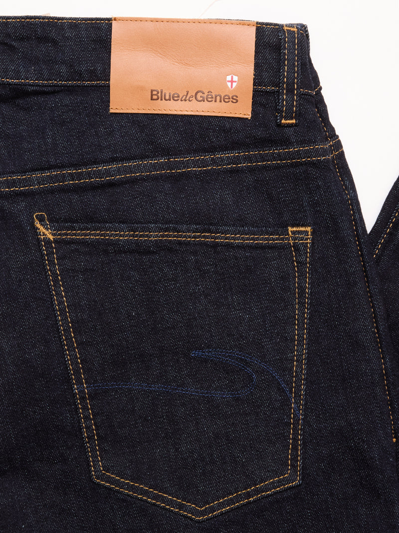 Close-up of the back pocket on Blue de Gênes Recco F V2 Jeans in a rinse wash, featuring yellow stitching and a tan leather patch with the brand name and a small red and white cross emblem above the pocket.