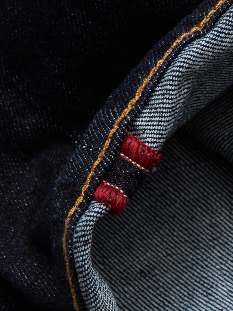 Close-up of Blue de Gênes Recco F V2 Jeans - Rinse Wash, highlighting the raw denim selvedge with a white and blue striped interior, red stitch, and contrasting orange stitching on the dark blue exterior.