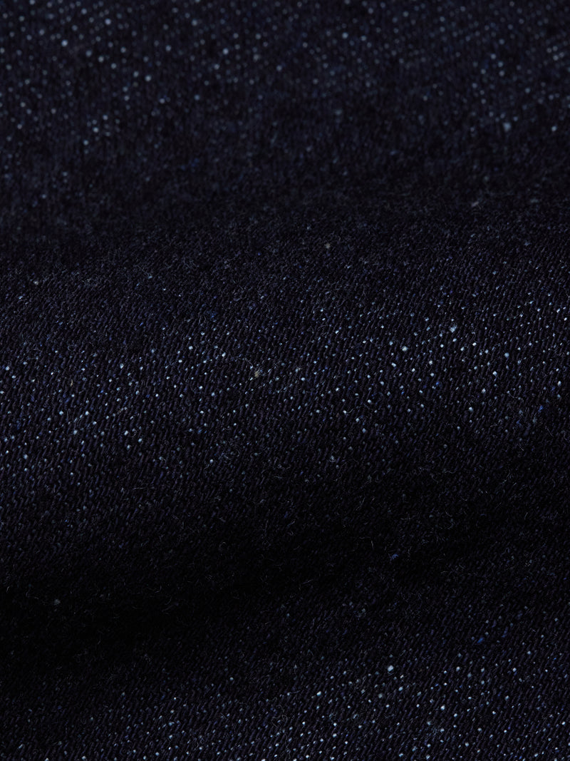 A close-up of the Recco F V2 Jeans - Rinse Wash by Blue de Gênes, showcasing dark blue denim fabric with a textured weave and fine white specks throughout.