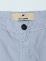 Close-up of the waistband on BGmenzo Vecchio Chino - Blue Fog by Blue de Gênes, highlighting a stitched label with a red and white shield above the brand name and a black button closure.