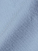 Close-up of Blue de Gênes BGmenzo Vecchio Chino in Blue Fog, featuring light blue fabric with a subtle ribbed texture and diagonal folds, highlighting the shaded drape typical of comfort stretch chinos.