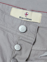 Close-up of BGpaulo Teo Pant in flint gray by Blue de Gênes, showing metal buttons with a shield emblem and a fabric label reading Blue de Gênes beneath a red and white cross logo.