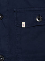 Close-up of the BGpontus Teo Overshirt by Blue de Gênes in dark navy textured cotton, featuring black buttons, a relaxed-fit breast pocket, and a small white tag with red cross and blue border on the pocket flap.