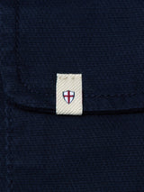 A close-up of the BGpontus Teo Overshirt in Dark Navy by Blue de Gênes shows a textured cotton pocket with a small beige tag featuring a red cross on white, evoking the flag of England.