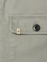 Close-up of the BGpontus Teo Overshirt in Shadow Green by Blue de Gênes, highlighting its textured cotton pocket with a black engraved button and a small beige tag featuring a red and blue shield design.