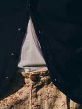 Close-up of a person wearing a dark cardigan over a white T-shirt, paired with Blue de Gênes BGcupra Print Shorts—multi-patterned relaxed fit shorts in beige and brown, featuring a visible waistband button.