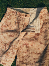 A pair of Blue de Gênes BGcupra Print Shorts - Multi Pattern, wide-fit camo style with button and zipper fly, shown open on green grass in sunlight.