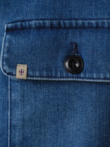 Close-up of the BGpontus Denim Overshirt - Used by Blue de Gênes, showing a blue cotton blend pocket with flap, black button, and small beige tag with red and blue shield emblem.