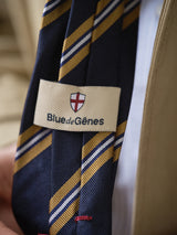 A close-up of the BGponsy Tie - Dark Navy by Blue de Gênes, featuring a red and white shield emblem, worn with a beige jacket and white shirt.