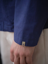 A close-up of a hand wearing the BGcanopy Jacket in Navy Peony by Blue de Gênes, featuring a small tag with a red and white shield, paired with light-colored pants.