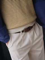 A person wearing Blue de Gênes BGpalco Twill Pants in Chalk with hands in pockets, a brown belt, a yellow and white striped sweater, and a Blue de Gênes blue jacket. The image shows only the torso and upper legs.