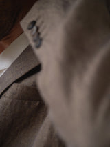 Close-up of a person wearing the BGcricket Lin Blazer in Grey Mel by Blue de Gênes, featuring a relaxed fit. The image highlights the fine linen-hemp blend texture on the lapel and shoulder, with part of the wearer’s neck and jawline visible.