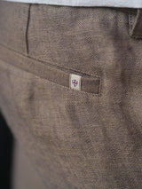 Close-up of the back pocket of Blue de Gênes BGpalco Lin Pants in Grey Mel, featuring a small cream tag with a red and blue shield emblem sewn near the pocket seam.