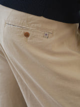 Close-up of a person wearing Blue de Gênes BGcopple Rodas Shorts in pale khaki, featuring a brown buttoned back pocket and a small white tag with a red and blue emblem. The person is also wearing a dark top.