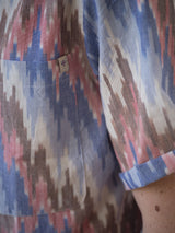 A close-up of a person wearing the Blue de Gênes BGponti Kala S/S Shirt, featuring a 100% cotton multi-color abstract zigzag pattern and a front pocket with a white tag showing a purple shield logo.